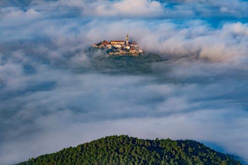Ancient town Buzet with bell tower and old buildings flying above clouds. Unusual landscape of tourist destination in Istria, Croatia © Mny-Jhee/Shutterstock